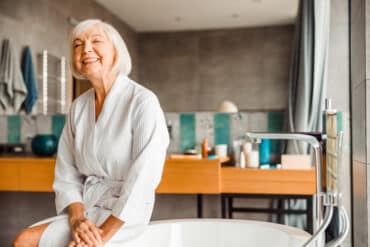 Elderly woman sitting next to bath tub.