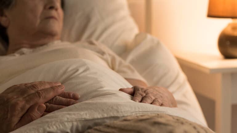 older woman in bed with a comforting hand over hers
