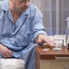 Old man sitting in pajama on bed with pills in bowl on night table