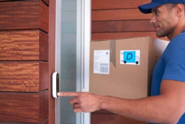 Package delivery man ringing a video doorbell at a residential front door